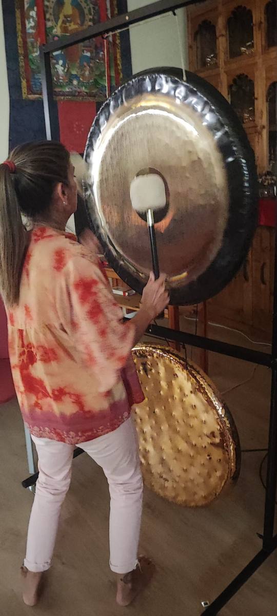 Montse playing the gong beside a thangka